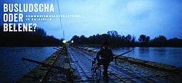 Das Foto zeigt die Pontonbrücke zur Insel Belene. Im Vordergrund schiebt ein Mann ein Fahrrad. Das Wetter ist düster.